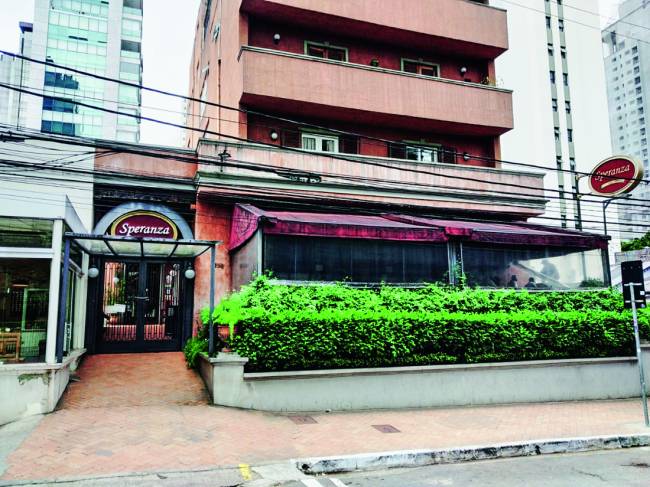 Fachada de prédio com jardim avarandado na frente e pizzaria Speranza no térreo.