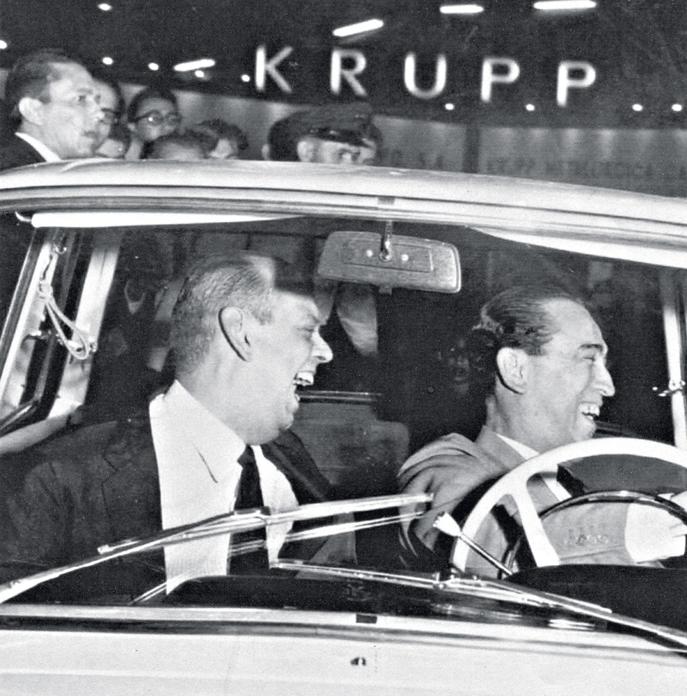 img102.jpg A imagem mostra Caio de Alcântara Machado e Juscelino Kubitschek dentro de um carro, com Juscelino no volante e os dois rindo ao olhar à direita.