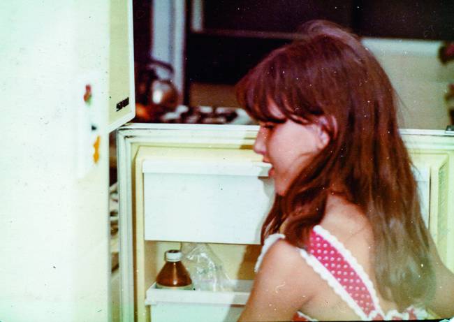 Menina (Paola) abrindo porta da geladeira.