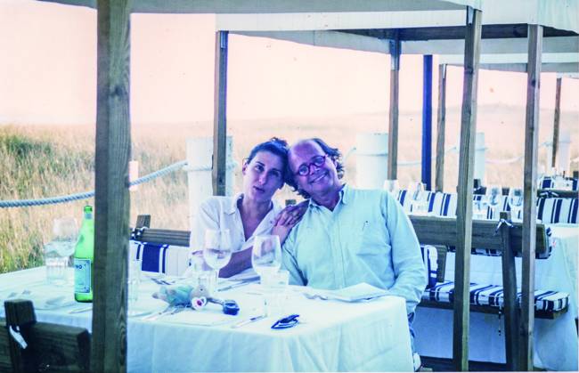 Mulher (à esquerda) e homem sentados abraçados em mesa de restaurante.