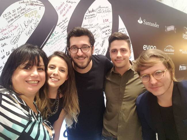 Helena Manosso Cinco pessoas (duas mulheres no canto esquerdo e três homens à direita) reunidas em frente ao painel de 20 anos de Comer & Beber.