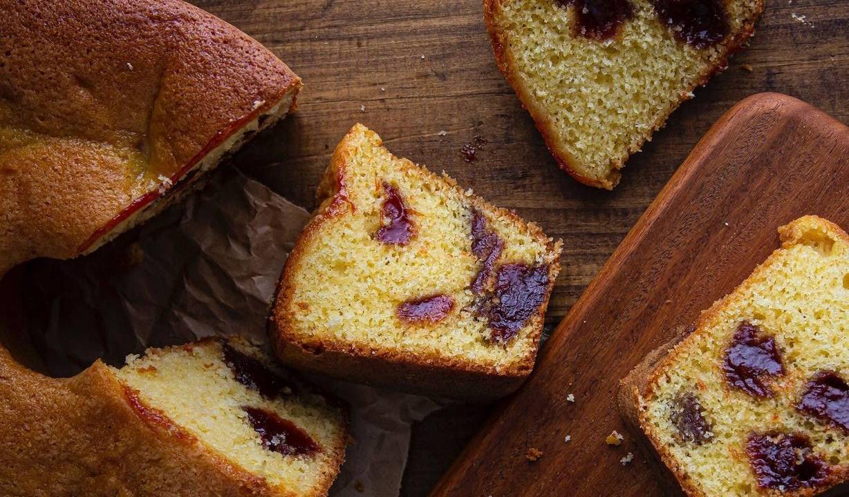 Bolo de fubá com goiabada semi cortado ao lado de fatias em tábua de madeira.