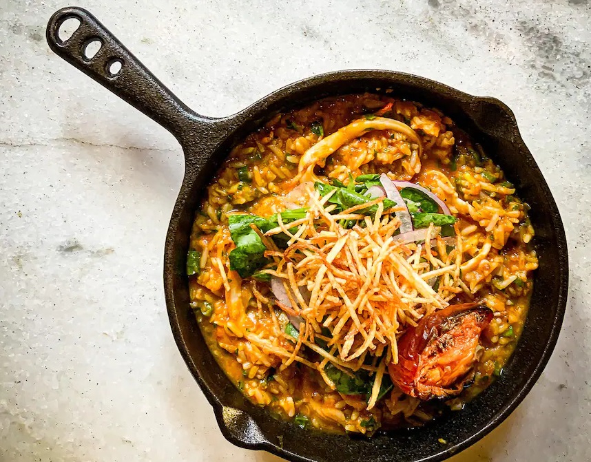 Foto aérea de frigideira de ferro com arroz cremoso com abóbora coberto por batata palha.