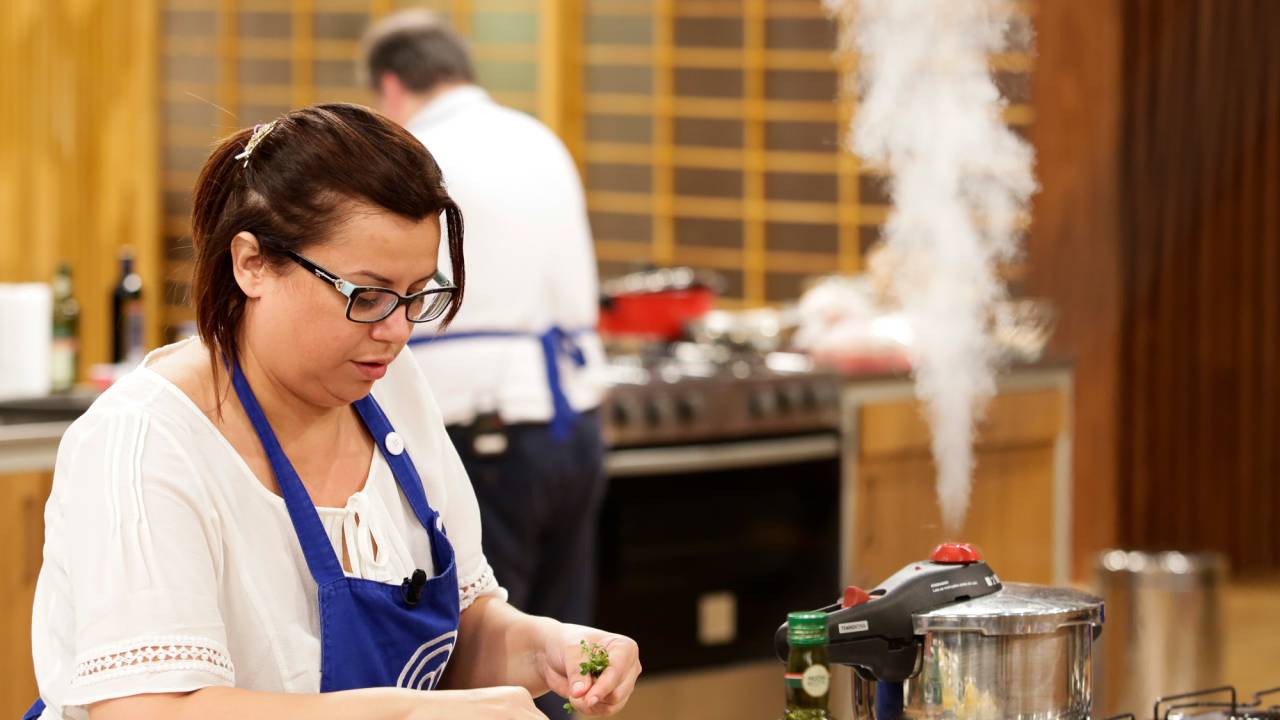 Helena Manosso no canto esquerdo cozinhando em bancada do MasterChef.