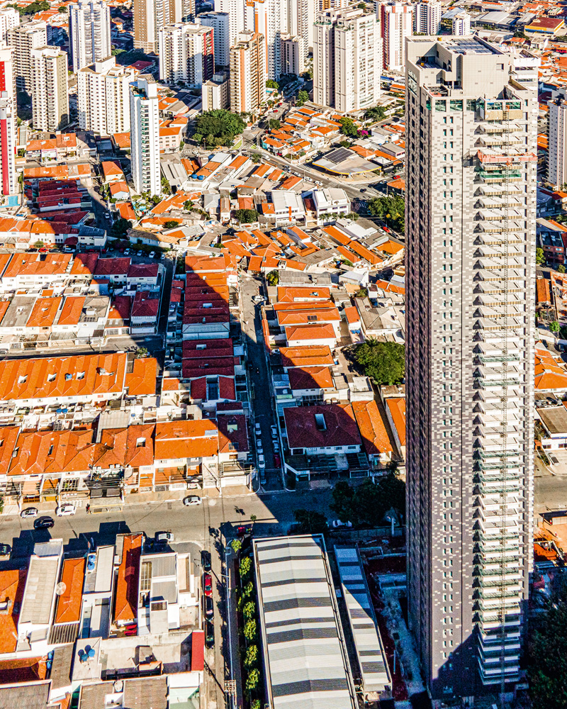 A imagem, vista de cima, mostra o prédio da região do Tatuapé cobrindo diversas casas com sua sombra extensa.