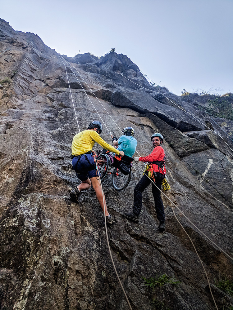pedreira-dib-imbróglio-ambiental-mairiporã-escalada.jpg imagem de precipício da pedreira com pessoas o escalando, dois instrutores auxiliando um cadeirante