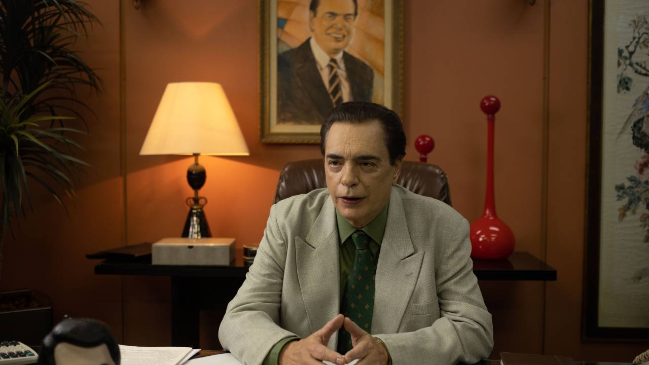 O ator José Rubens Chachá, sentado em sua mesa, em cena da série O Rei da TV