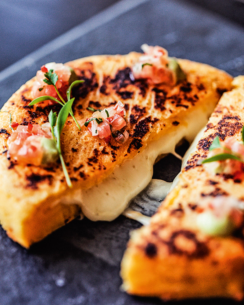 SALTAS&TAPAS – AREPA QUEIJO.jpg.jpg Arepa cortada ao meio, com queijo derretido e sendo mostrado.