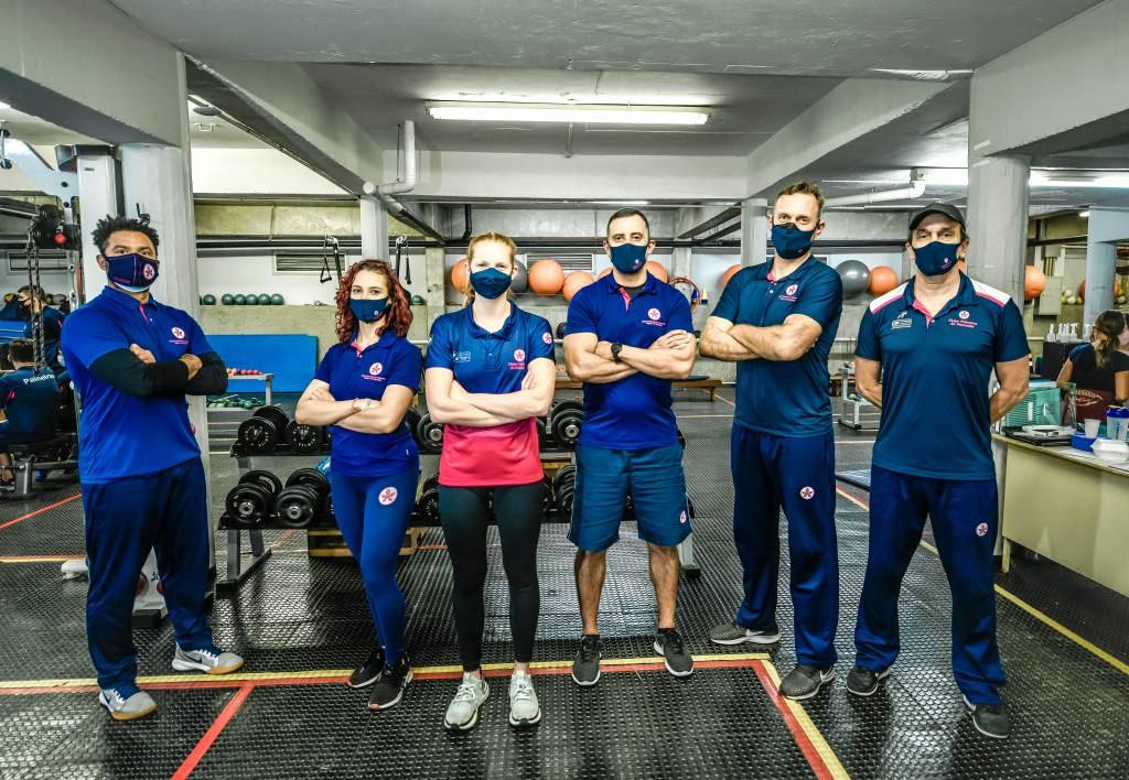 STEPHANIE_21 A imagem mostra Stephanie e outras pessoas com uniforme do Paineiras em uma academia, todos de máscara e braços cruzados
