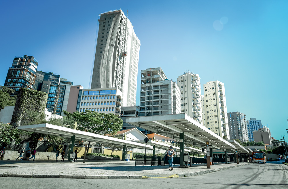 A imagem mostra prédios atrás da Vila Madalena, alguns ainda em construção. A perspectiva é de dentro do terminal de ônibus.