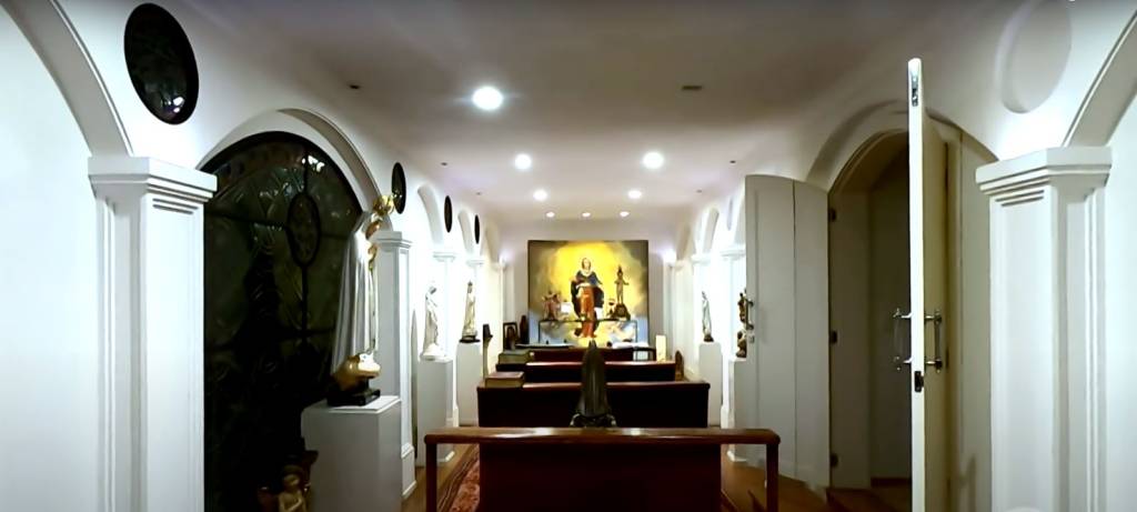 casa-hebe-camargo-capela2 os bancos da capela no centro, o altar ao fundo e as paredes que cercam a capela com estátuas sacras