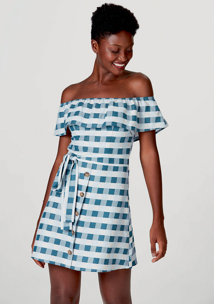 Mulher negra sorri e olha pra baixo vestida com vestido azul e branco xadrez