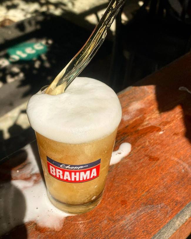 Foto de chope Brahma sendo tirado sobre mesa de madeira.