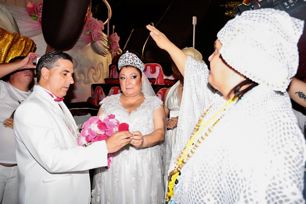 sérgio e angelina de mãos dadas enquanto pai de santo realiza cerimônia com o braço levantado