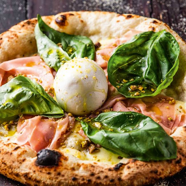 Pizza de presunto cru com folhas grandes de manjericão e burrata.