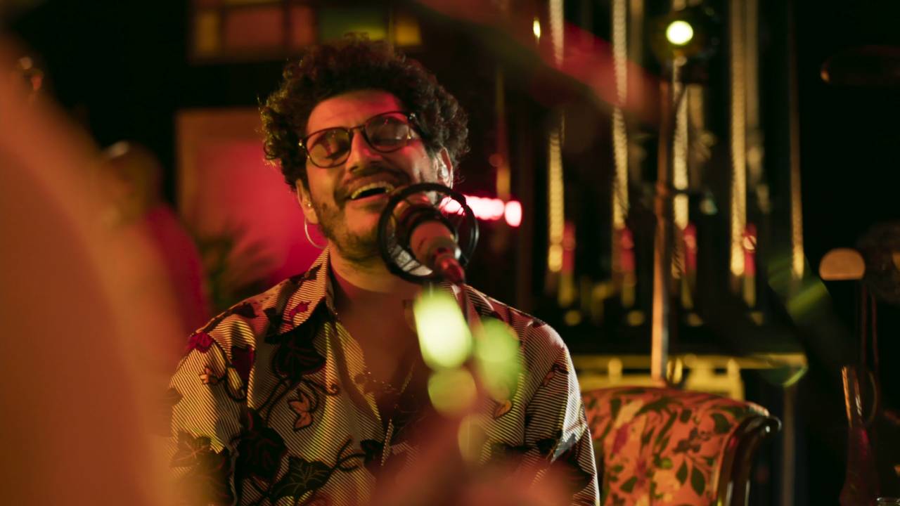 Cantor Criolo cantando sentado de olhos fechados.