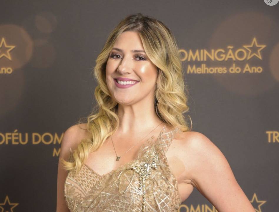 Dani Cabalresa posa de vestido dourado e cabelos loiros. Sorri para a câmera e ao fundo aparece a frase "Domingão Melhores do Ano"