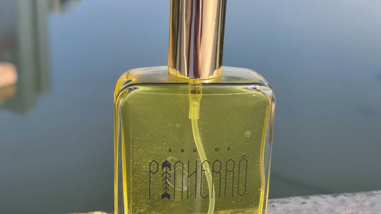 A foto exibe frasco de vidro com líquido amarelo depositado em superfície em frente ao Rio Pinheiros, que aparece no fundo.