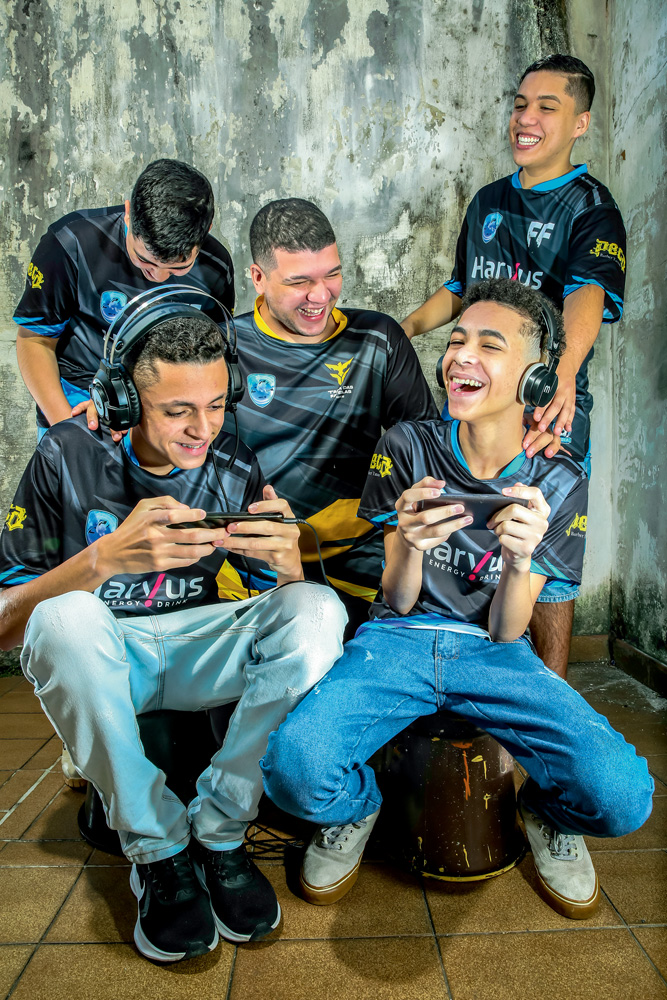 Equipe Cufa: Cauê, Felipe, Nycolas, Davi e Ryan Barbosa A imagem mostra Cauê, Felipe, Nycolas, Davi e Ryan Barbosa, todos rindo enquanto jogando Free Fire no celular. Todos estão com o uniforme preto da equipe.