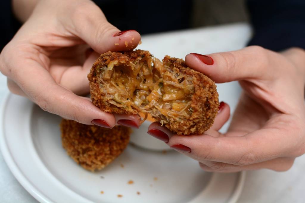 Cepa Mãos brancas de unhas pintadas de vermelho partindo croqueta de carne ao meio.