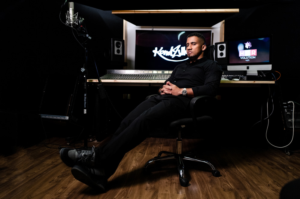 KondZilla-Konrad-Dantas A imagem mostra Konrad, sentado em uma cadeira dentro de um estúdio. Há, ao fundo, um enorme mesa de mixagem de som e um telão ao fundo escrito KondZilla.
