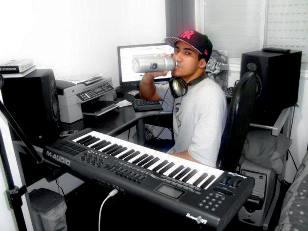 KondZilla-Konrad-Dantas A imagem Konrad em um quarto. Ele está sentado, e em volta há um teclado, caixas de som, uma impressora e seu computador.