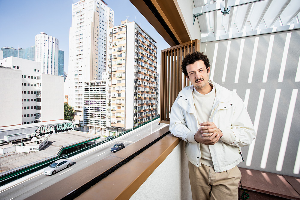 Na vista, é possível ver alguns prédios "retrofitados" A imagem mostra Guil com o cotovelo sobre uma janela. Na vista, é possível ver alguns prédios.