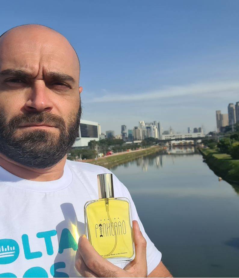 Marcelo Reis, porta-voz Volta Pinheiros (DIVULGAÇÃO) Marcelo Reis, porta-voz do movimento Volta Pinheiros, segura frasco de líquido amarelo em frente ao Rio Pinheiros. Ele é careca e tem barba.