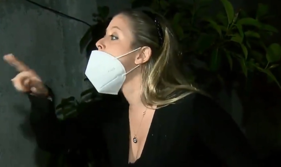 A imagem mostra a mulher, com a máscara deixando o nariz de fora, apontando o dedo para o câmera da Record