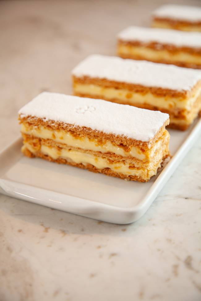 iFood Gourmet – Confeitaria Dama Três mil-folhas postos em diagonal sobre prato retangular de louça branca.