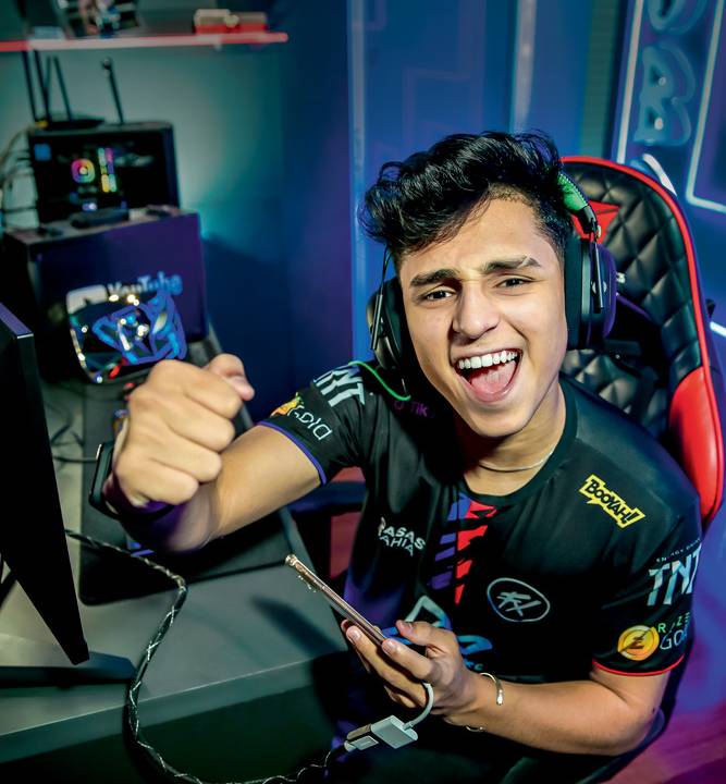 A imagem mostra Bruno "Nobru" Goes sentado em uma cadeira gamer, com uniforme e comemorando para a câmera.