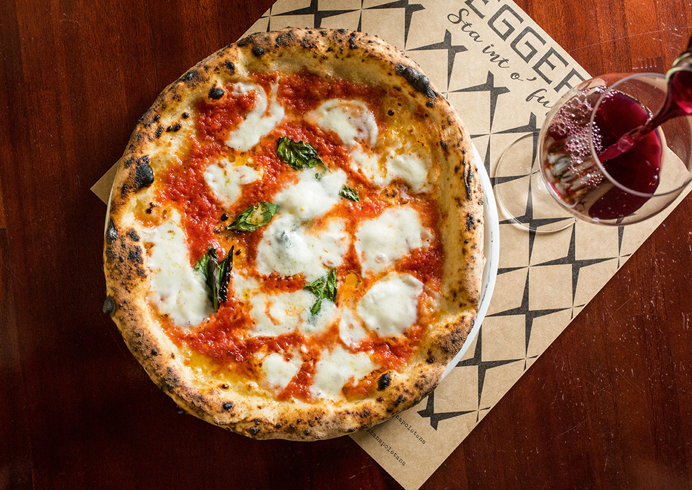 Foto aérea de pizza margherita ao lado de taça de vinho tinto.