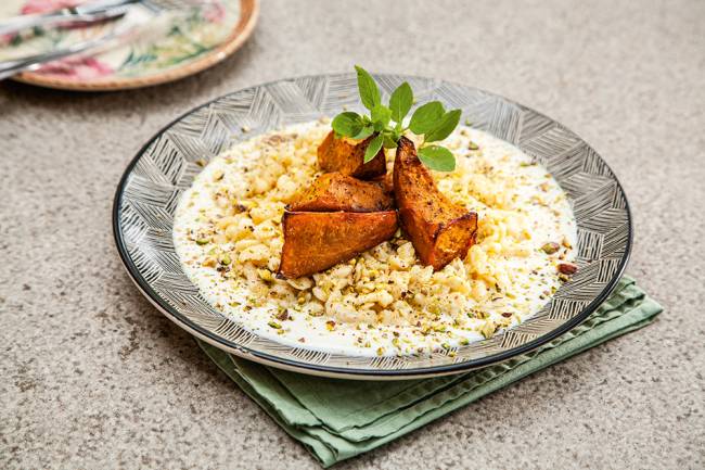 Gansaral Spätzle coberto por três pedaços de abóbora-cabotiá assada e ramo de manjericão.