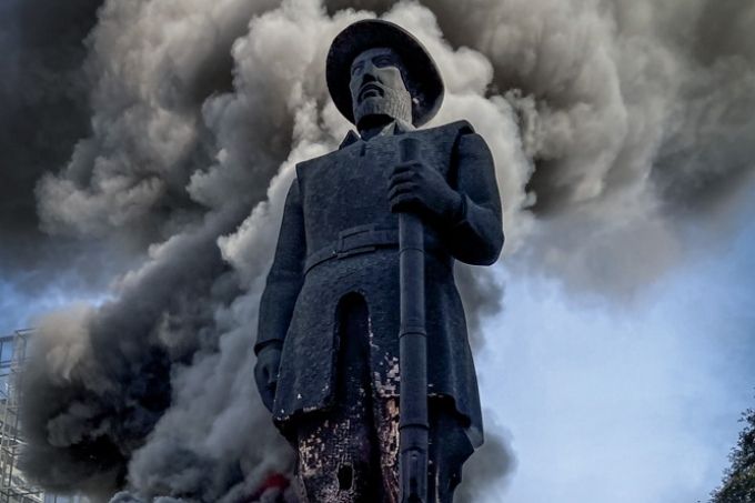 estátua de borba gato com fumaça preta saindo da estrutura por conta de labaredas de fogo na base e pernas