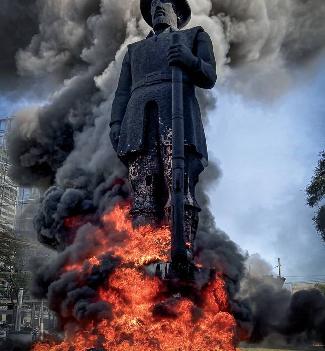 estátua de borba gato com labaredas de fogo na base e pernas com fumaça preta saindo da estrutura