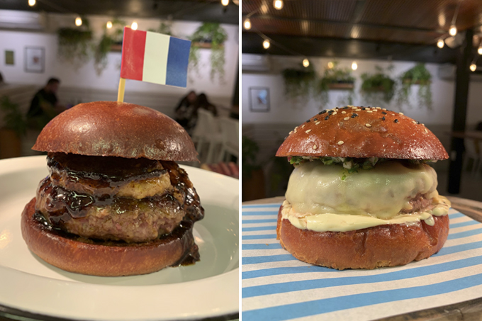 Duas imagens verticais unidas por linha fina branca. À esquerda hambúrguer alto com bandeirinha da França por cima. À direita, hambúrguer alto coberto por queijos sobre papel listrado azul e branco.