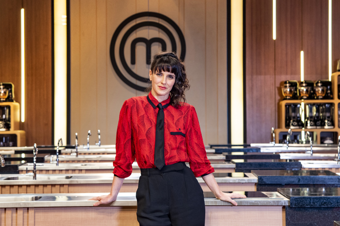 Chef Helena Rizzo de camisa vermelha e calça preta encostada na bancada de cozinha do MasterChef.