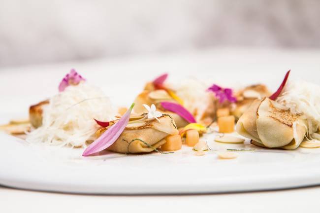 Falso tortelli de pupunha da chef Helena Rizzo sobre prato plano de louça branca.