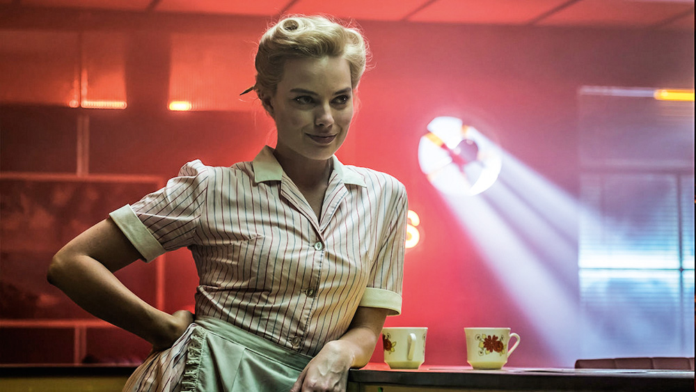 margotrobbie2.jpg A imagem mostra Robbie sorrindo, com o braço apoiado em um balcão onde há um xícara.