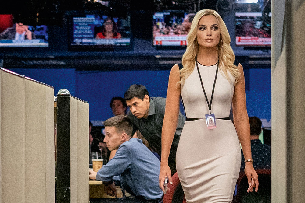 margotrobbie3.jpg A imagem mostra Margot Robbie em uma redação televisiva enquanto caminha por ela, com um crachá.