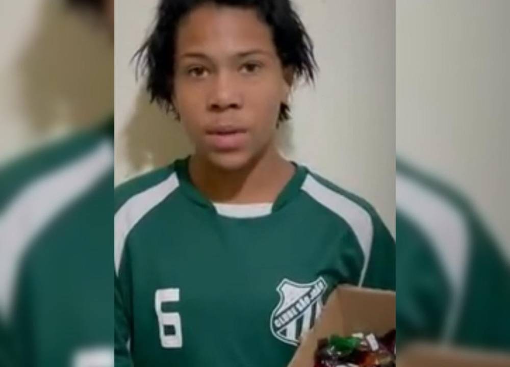 joao victor está com expressão séria para a câmera segurando uma caixa com trufas dentro. ele está com o uniforme verde do clube são joão