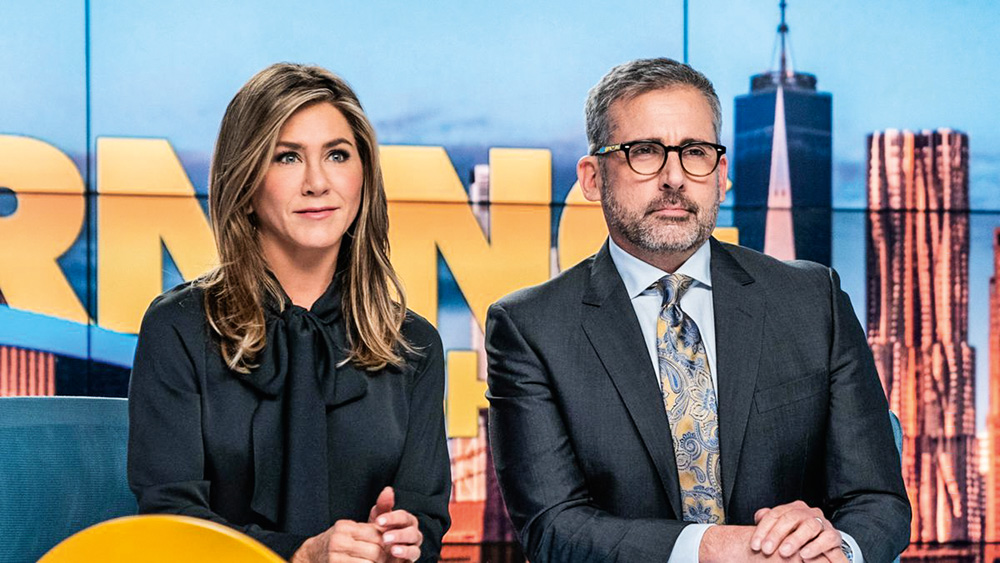 A imagem mostra Jennefir Aniston e Steve Carell em uma bancada de jornal televisivo, olhando para frente, durante a série The Morning Show