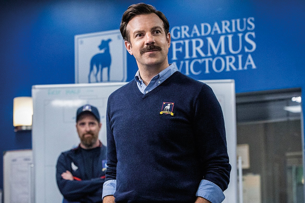 tedlassoapple_divulgacao.jpg A imagem mostra o ator Jason Sudeikis, na série Ted Lasso, com um suéter com bordado do clube no qual é treinador e ele olhando para o vestiário onde está seu time