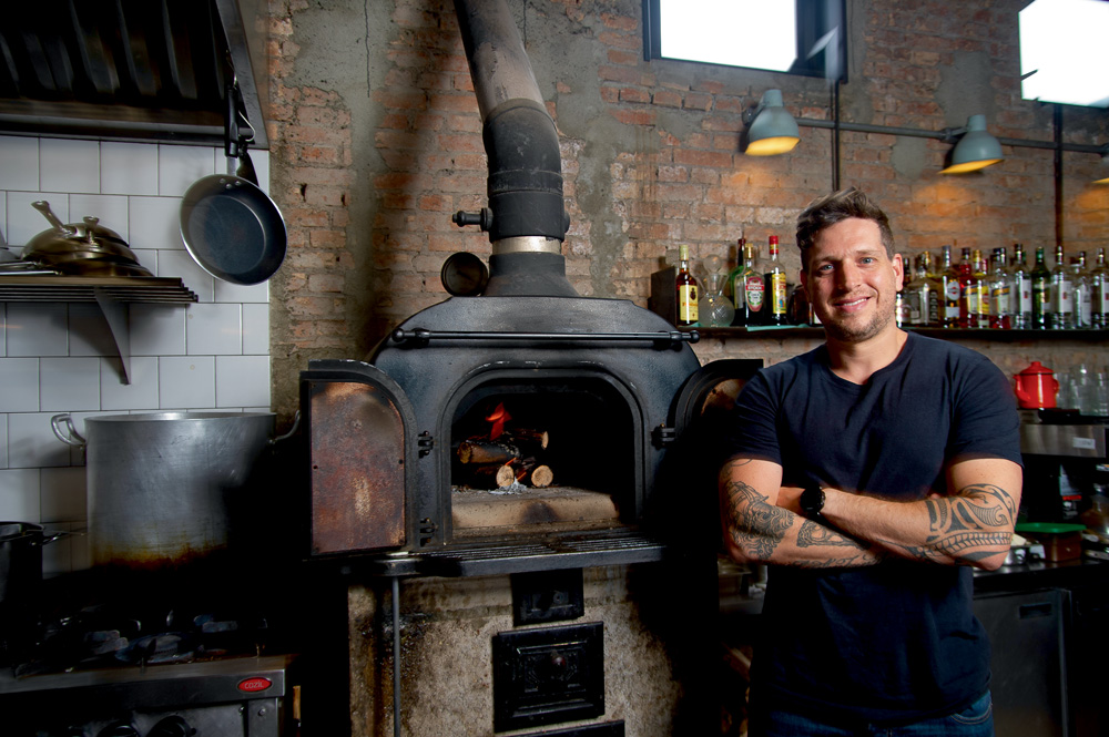 Chef Fellipe Zanuto ao lado de forno a lenha.