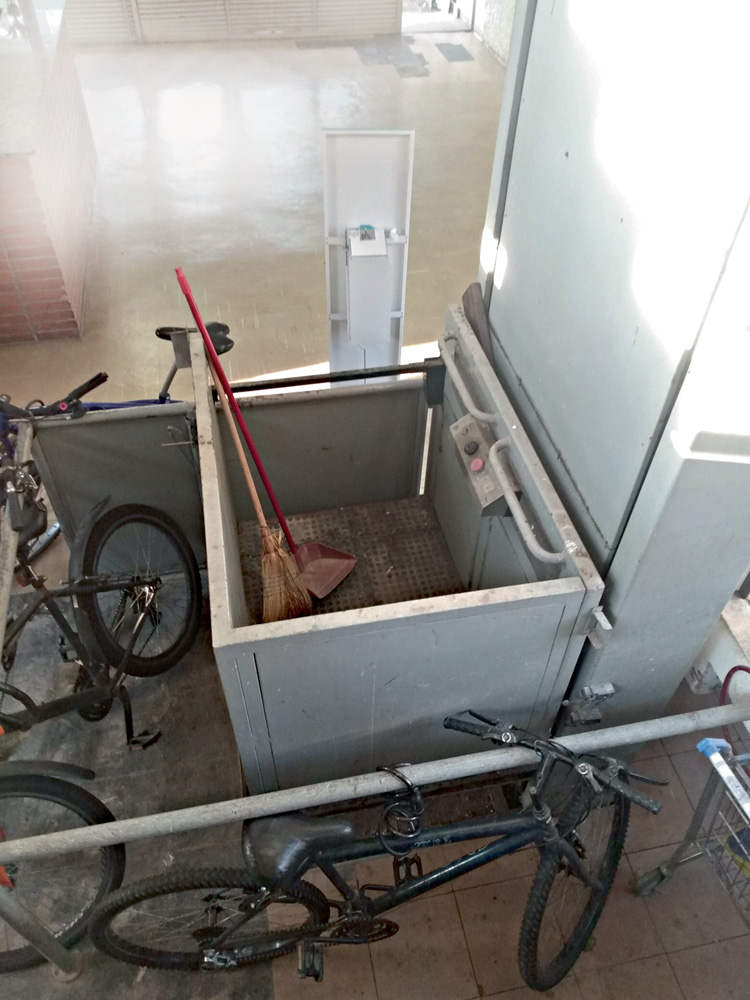 Elevador para cadeirante que não funciona.jpg Um elevador visto de cima. Há bicicletas ao lado da estrutura, que está aberta com uma vassoura dentro
