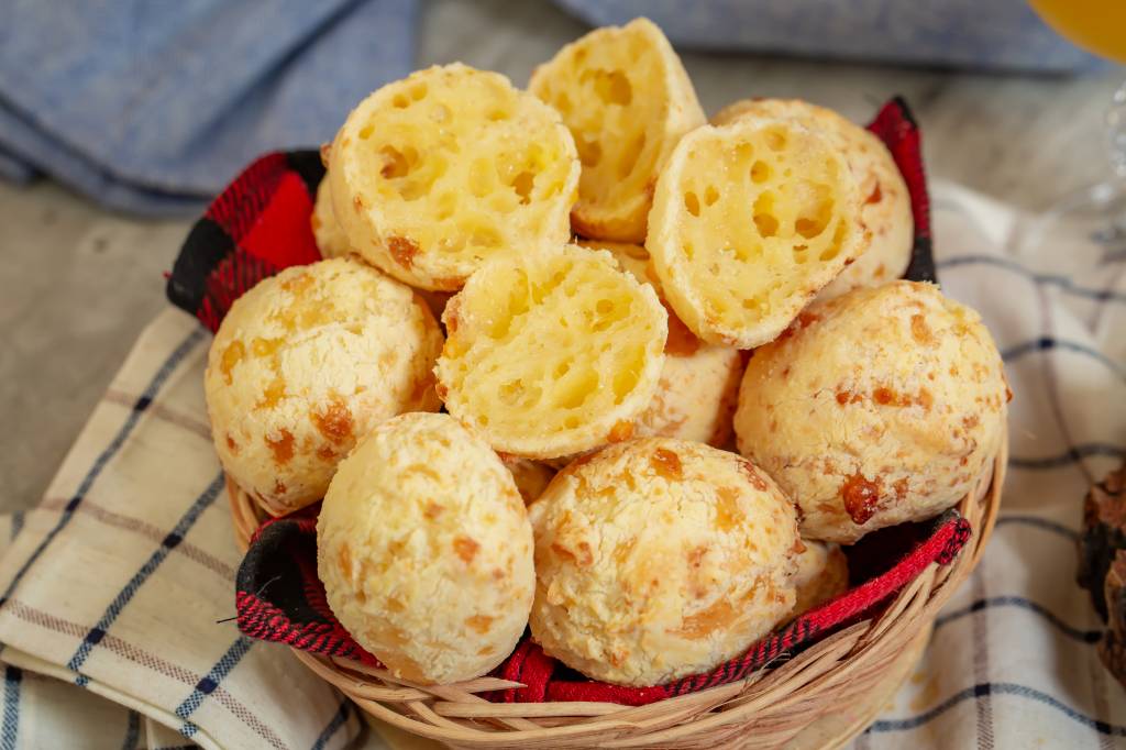 Taça de vidro com sorvete sobre base redonda de madeira, com pedaço de goiabada, pedaço de queijo e pequena faca ao lado, sobre mesa de madeira branca