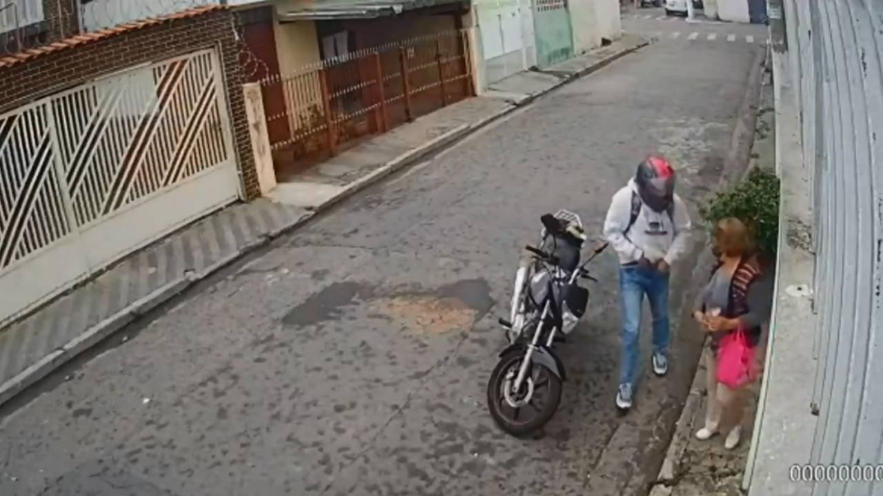 A imagem mostra uma pessoa de capacete, colocando a mão dentro da calça para pegar a arma. Na frente dela, há um idosa, com a bolsa na mão.