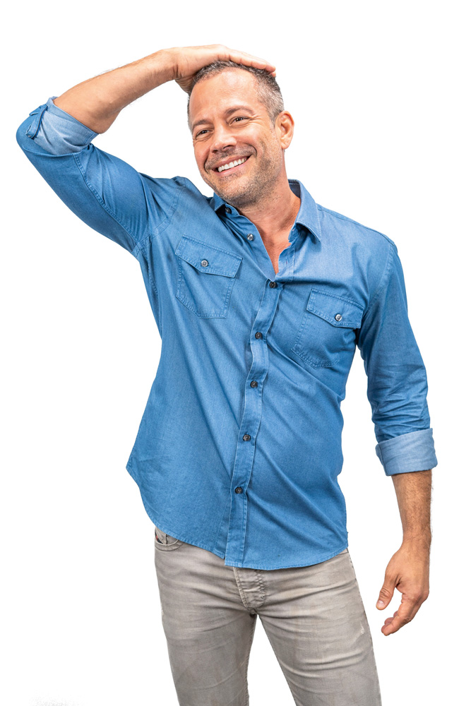 Malvino Salvador (Daniel Melo) Malvino Salvador põe uma das mãos na cabeça e sorri. Veste camisa jeans e calça clara.
