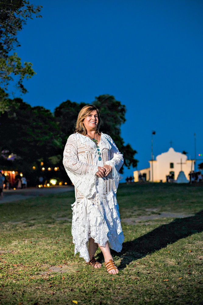 Martha Medeiros (ELLEM CARDOSO) Martha Medeiros aparece de pé em gramado durante a noite. Ao fundo, uma casa branca. Ela veste vestido inteiramente branco e tem cabelos castanhos claros. Posa segurando as mãos uma na outra.