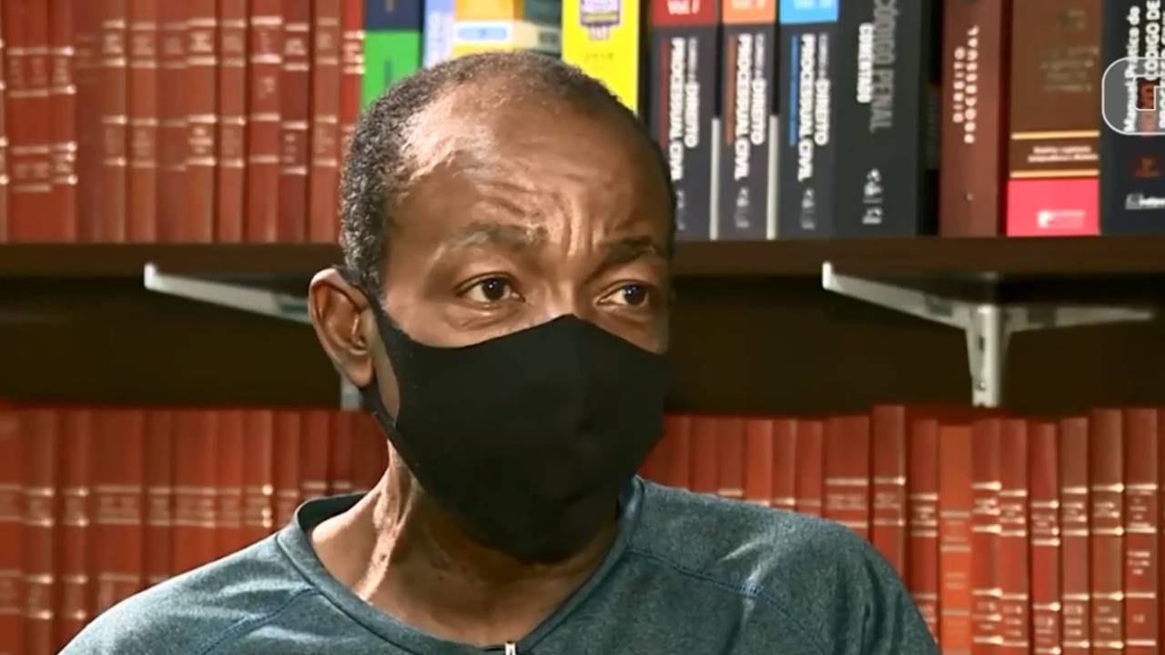 A imagem mostra Carlos da Silva, de máscara. É possível ver sua expressão nos olhos, séria, e o cabelo raspado.